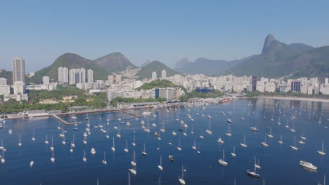 Sobrevuelo-Aéreo-De-Veleros-Anclados-En-La-Bahía-De-Botafogo-Con-La-Ciudad-Al-Fondo-En-Río-De-Janeiro,-Brasil