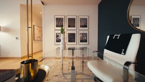 wide push in shot inside of a modern home office over a glass table with a white chair, glass walls, and art hanging on the wall