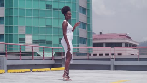 In-a-white-dress,-a-black-girl-is-on-a-rooftop-with-the-city-skyline-visible