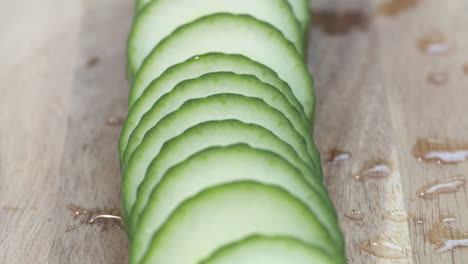 Close-up-pan-down-a-row-of-fresh,-ripe-slices-of-English-cucumber-on-a-wood-cutting-board