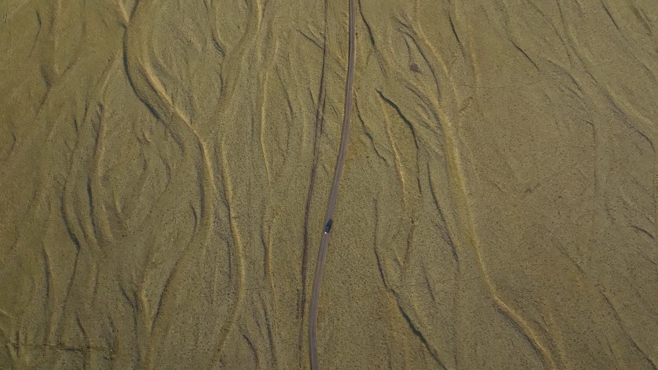 Aerial view of a car driving along a winding road through the textured golden plains of North Iceland, highlighting the unique natural patterns of the landscape.