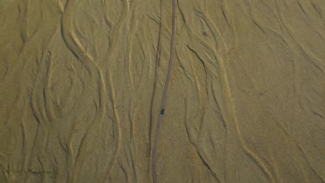 aerial view of a car driving along a winding road through the textured golden plains of north iceland, highlighting the unique natural patterns of the landscape.