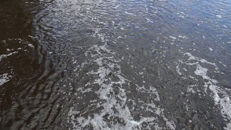 River-water-flowing-over-the-weir,-Canning-River---Perth-Western-Australia-Looking-down-onto-the-river-from-the-bridge,-bubbles-from-the-flowing-water-across-the-weir