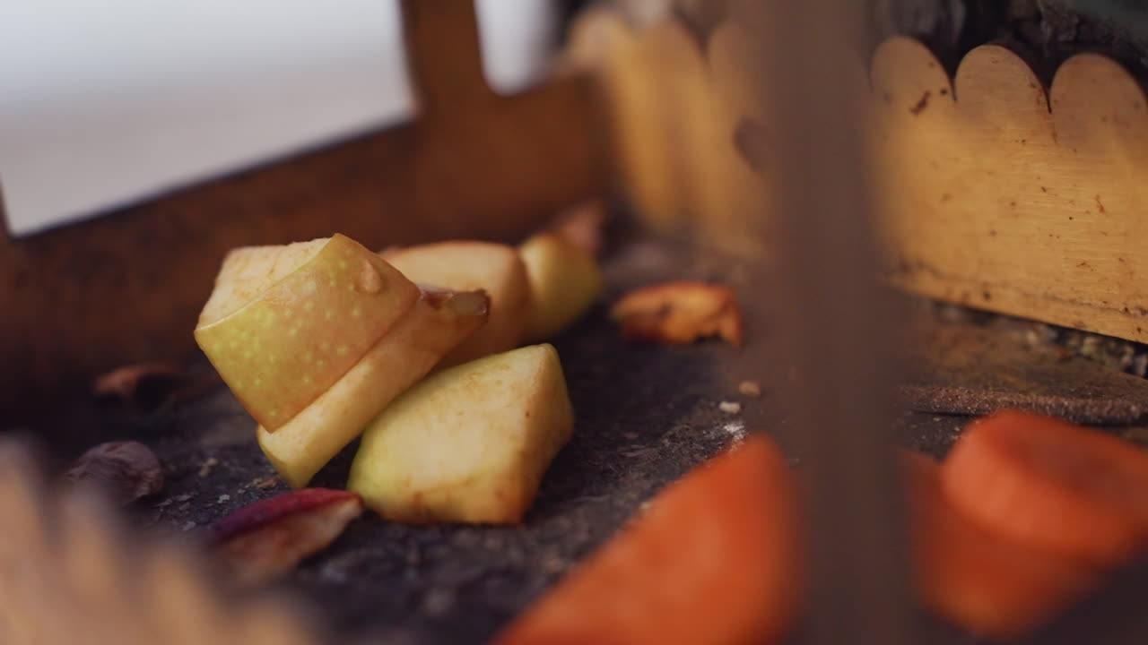 Close up of sliced fruits and vegetables including apples and carrots arranged inside wooden bird house, with smooth blurred background of motion and light giving calm natural outdoor setting
