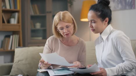 frau mittleren alters und weibliche finanzberaterin treffen sich zu hause, um einzelheiten des bankwesens und der buchhaltung zu besprechen und gemeinsam das budget zu verwalten