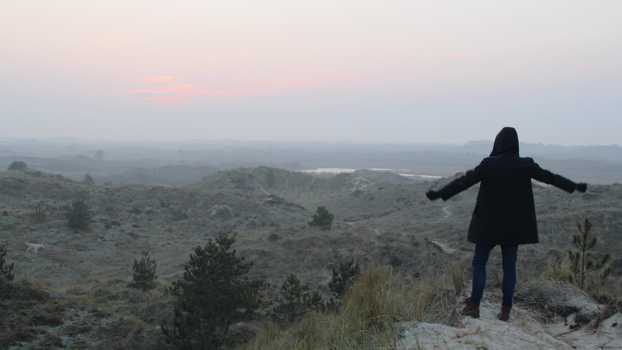 재킷을 입은 남자의 실루엣은 해가 지거나 해가 뜨면 산 정상에서 팔을 들어 올린다