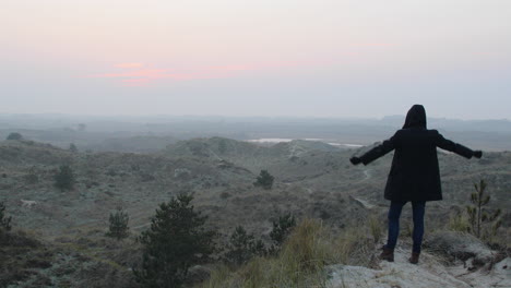 silhouette of a man with jacket raise arms in achievement on top of mountain at sunset or sunrise