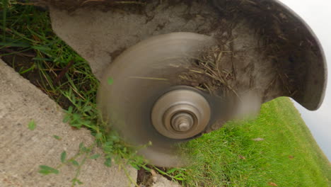 close-up pov of power edger blades trimming grass edge next to sidewalk