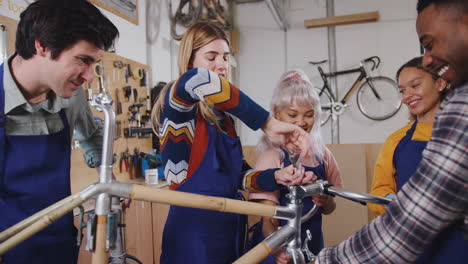 multi-cultural team of trainees in workshop learn how to assemble hand built bicycle frame together