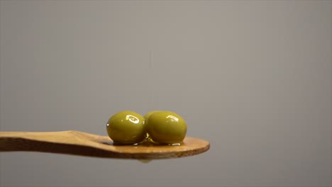 el aceite de oliva cae sobre las aceitunas colocadas en una cuchara de madera