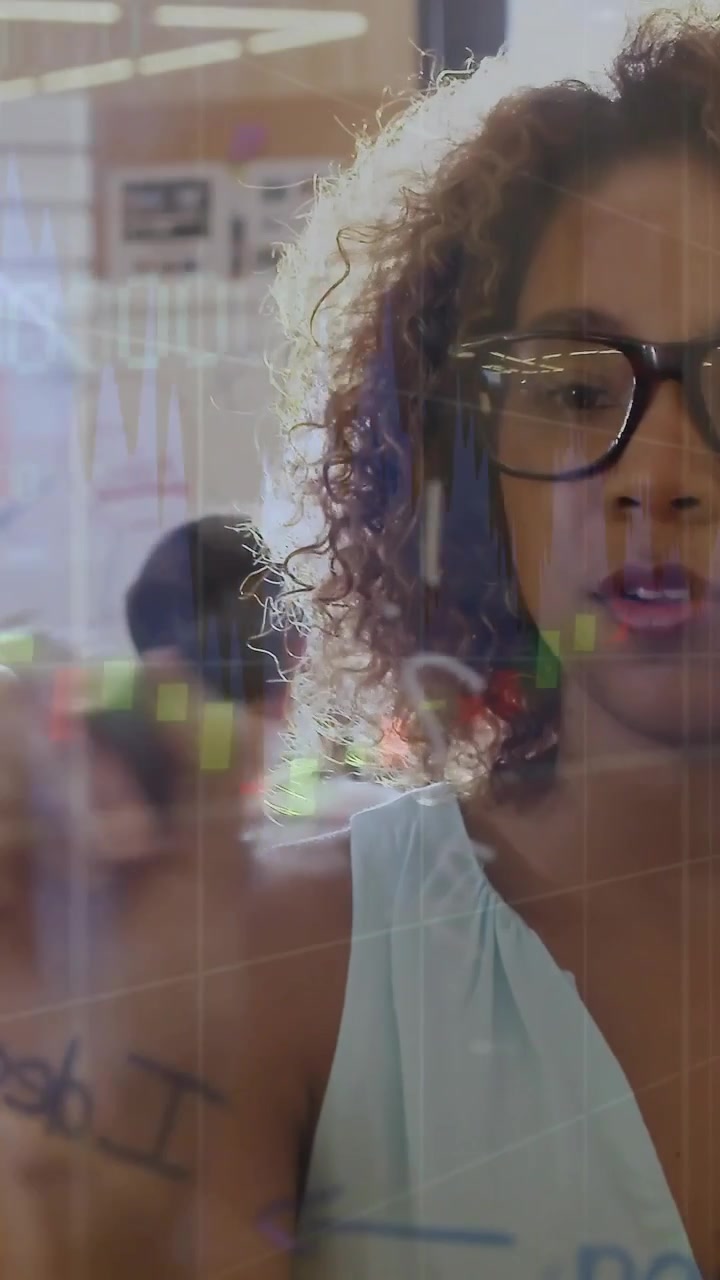 Vertical video: Woman raising marker to glass, annotating finance charts and showing trend to team
