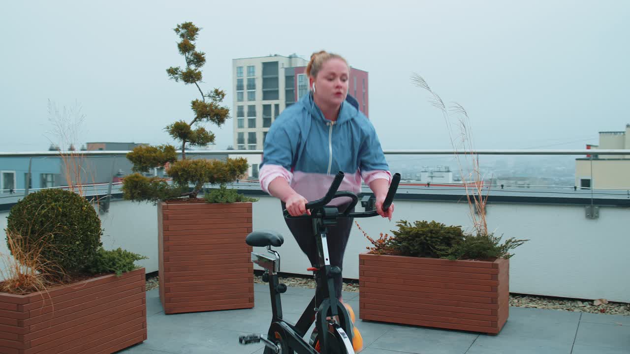 Athletic woman riding on spinning stationary bike training routine on house rooftop weight loss