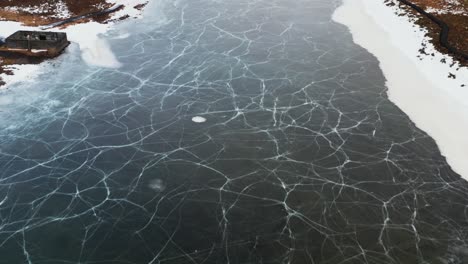 frozen seltjörn fishing lake in iceland during winter season with cracked surface, aerial