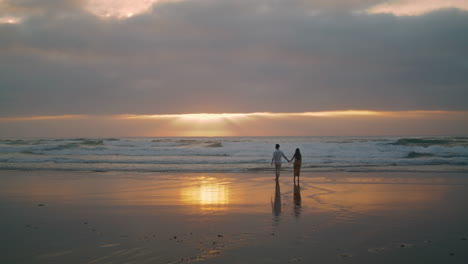 Silhouetten-Von-Liebenden,-Die-Durch-Sonnenstrahlen-Am-Meer-Spazieren.-Menschen,-Die-Ein-Date-Genießen,-Vertikale-Ansicht