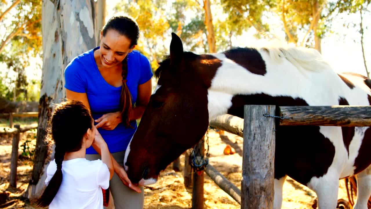 Mother and daughter stroking horse in ranch 4k