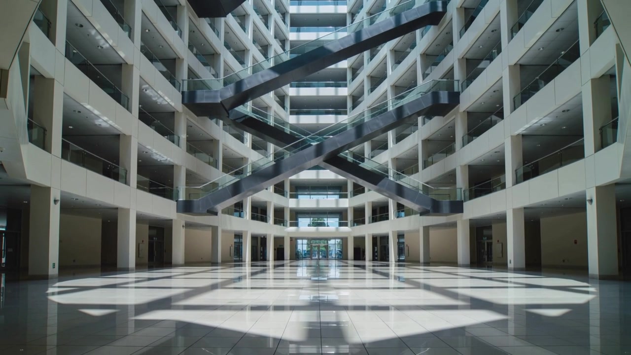Cámara avanzando revelando un atrio central de varios pisos, documentando la luz solar y escaleras mecánicas diagonales.