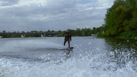 man riding wakeboard on wave of motorboat in summer river. active life