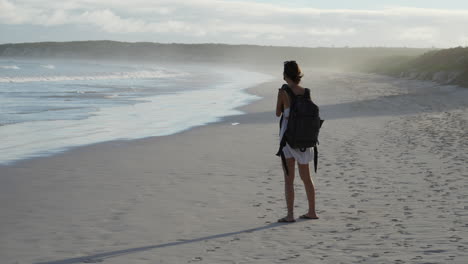 young female backpacker taking photograph of waves on tortuga bay in the galapagos