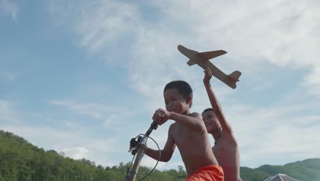 two boys riding a bicycle and playing with a paper airplane
