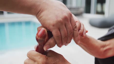 hands of adult asian daughter holding hand of senior mother sitting in garden holding walking stick