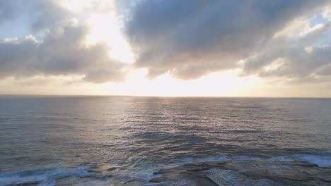 Aerial-rise-up-shot-reveals-a-beautiful-golden-sunrise-in-the-horizon-at-Dee-Why-Beach,-Nothern-Sydney,-NSW