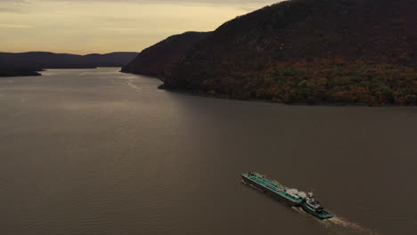 aerial-shot-over-a-turqiuse-colored-barge---tugboat-on-the-Hudson-River-on-a-cloudy-evening-in-Beacon,-NY