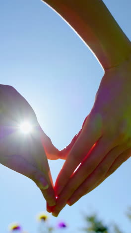 hands forming a heart shape against a bright sky