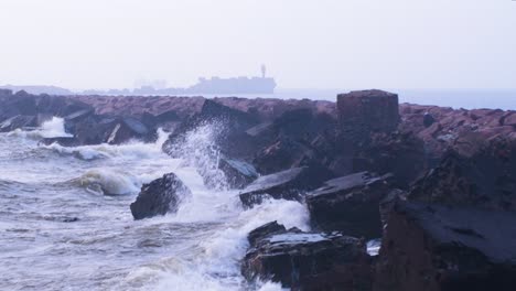 large cargo ship entering the port of liepaja in foggy day, stone pier in foreground, waves splashing, people walking on pier, distant medium shot