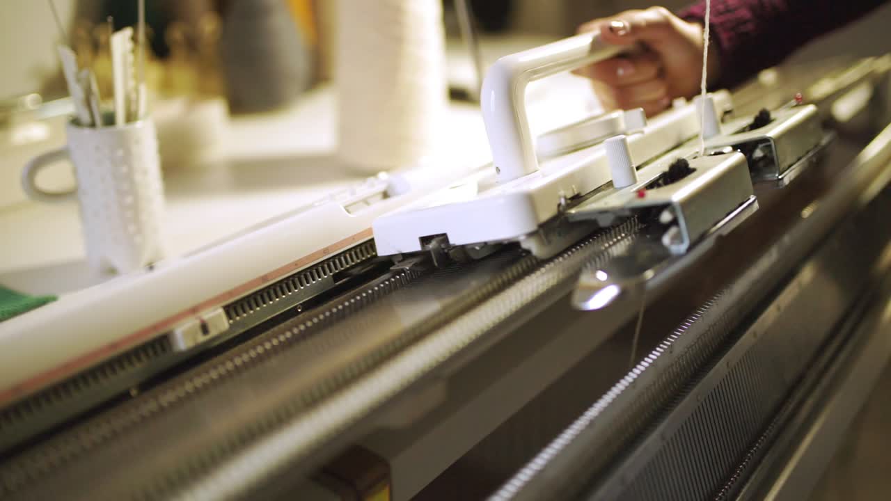 Creative woman making knitted texture on weaving machine in workshop