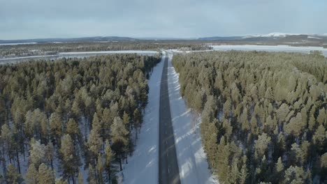 Drone-shot-flying-backwards-showing-road-in-between-forests-of-pinetrees-in-Northern-Sweden