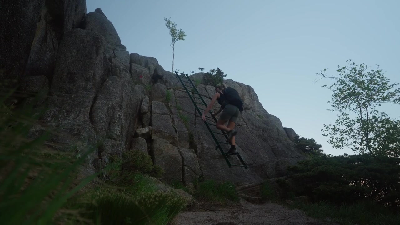 Donna caucasica con zaino sale una scala fissata a un fianco di montagna di granito durante un'avventura escursionistica impegnativa nei paesaggi selvaggi della Norvegia.