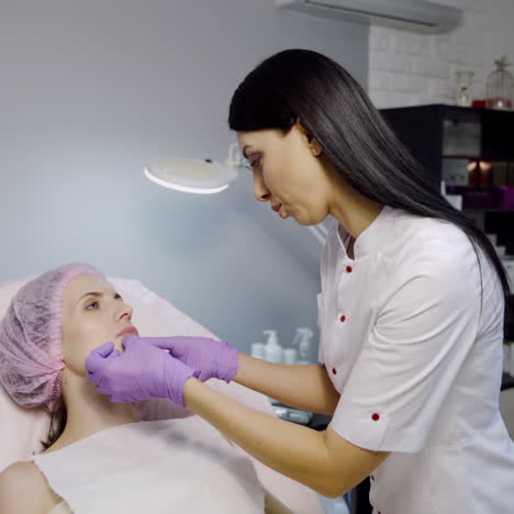 a pretty cosmetologist is looking over a shape of the client's lips and consults her before performing the procedure for lip augmentation in the cosmetology center.