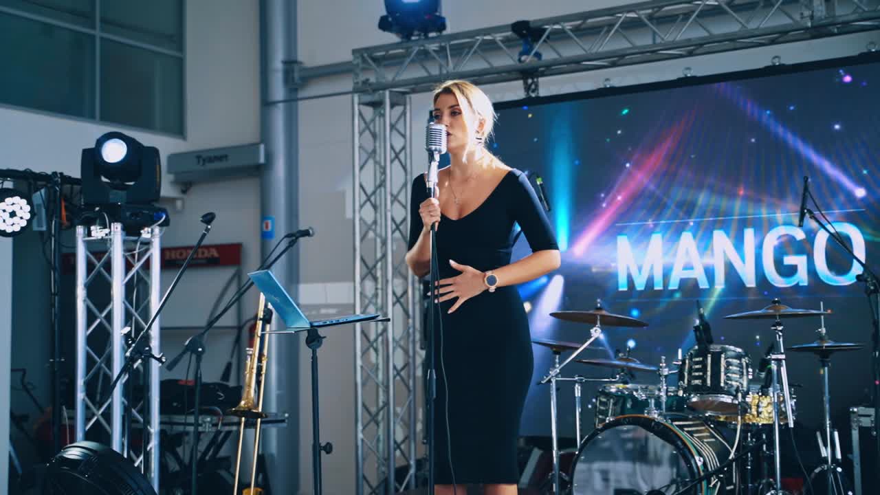 Woman singer on the modern scene in the daytime. Beautiful female in black dress singing into the microphone on a stage for special event.
