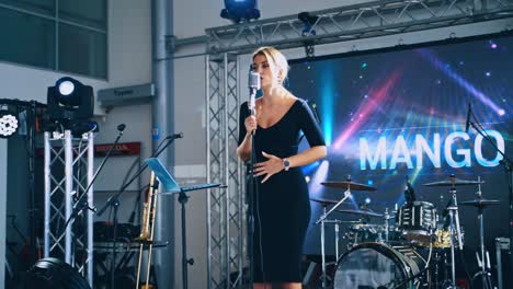 woman singer on the modern scene in the daytime. beautiful female in black dress singing into the microphone on a stage for special event.