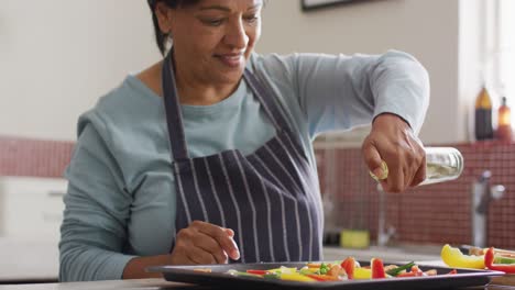 Asian-senior-woman-pouring-olive-oil-over-vegetable-salad-in-the-kitchen-at-home