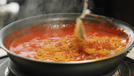 Chicken in tomato sauce is boiling on a frying pan with spices. Cooking tomato sauce curry with chicken fillet. Traditional Italian Mexican Asian dish. High quality studio shot for cafe, restaurant close up.