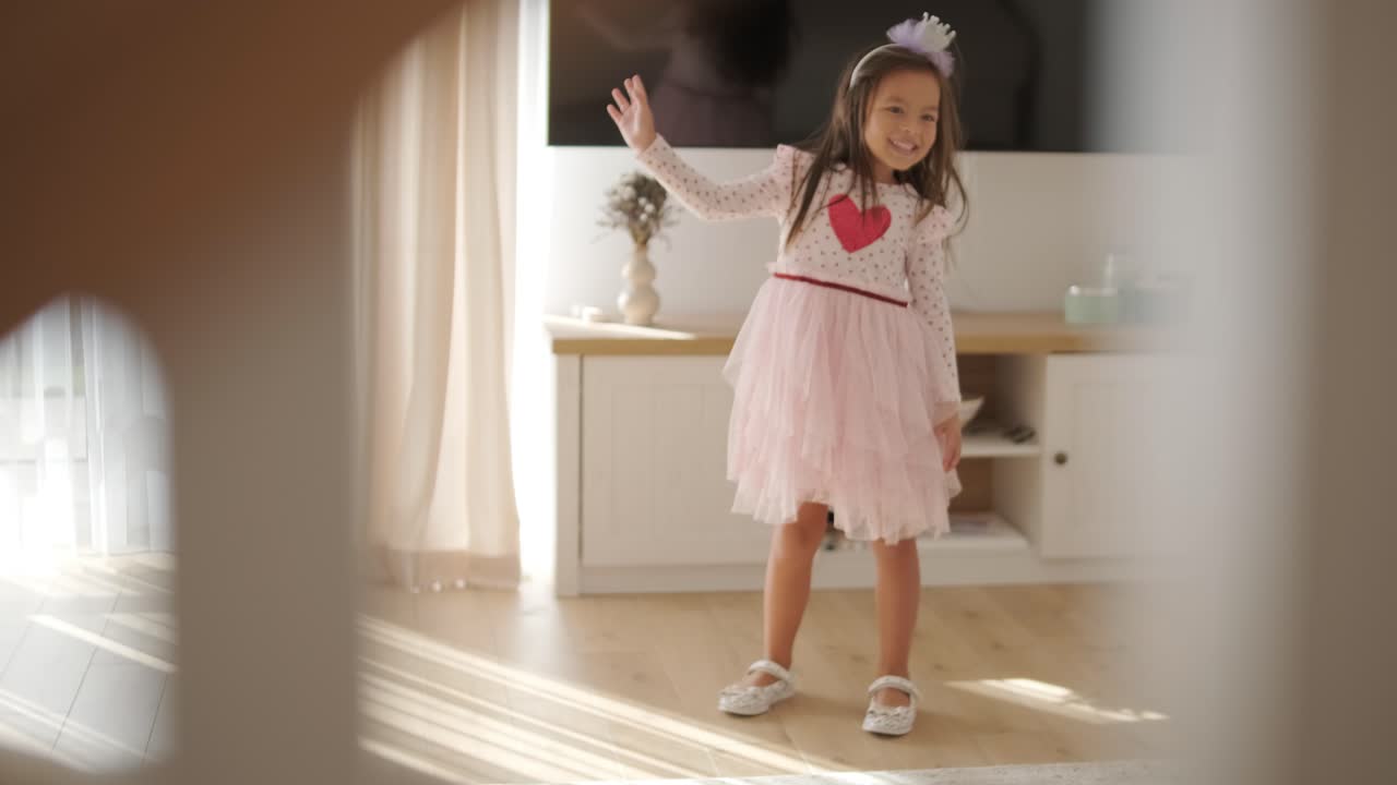 una joven baila alegremente en una sala de estar luminosa y acogedora. lleva un vestido rosado con un diseño de corazón, moviéndose juguetón en el espacio minimalista iluminado por el sol con decoración neutral y luz natural suave.
