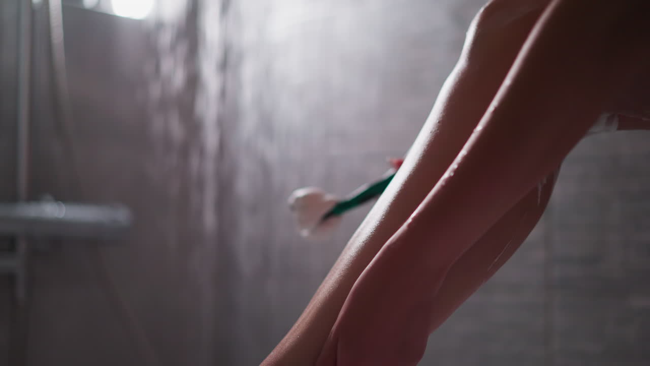 Woman strokes smooth leg in shower cubicle closeup. Lady enjoys soft body skin after shaving with razor in home bathroom. Spa care procedures