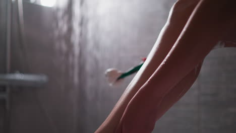la mujer acaricia la pierna lisa en un primer plano en el cubículo de la ducha. la dama disfruta de la piel suave del cuerpo después de afeitarse con la navaja en el baño de casa. procedimientos de cuidado de spa