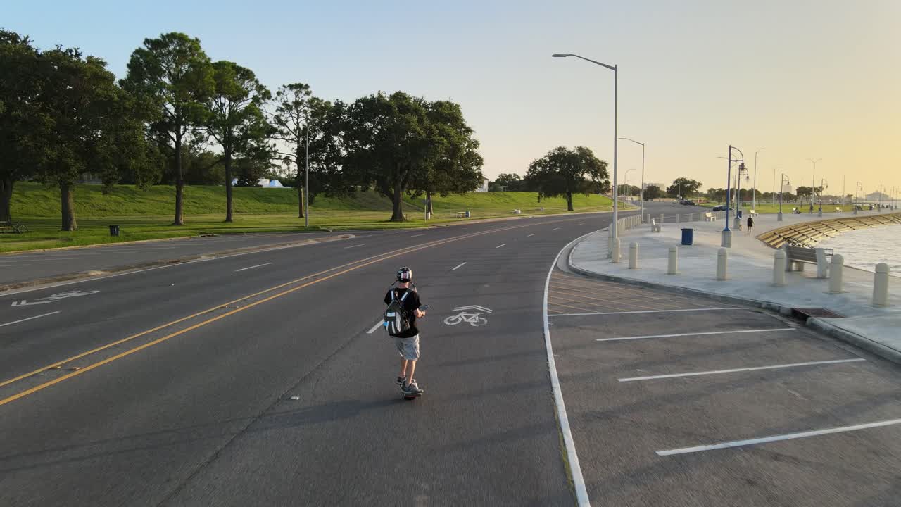 Young Man Strolling At Empty Lakeshore Drive With Electronic Skateboard At Dusk. - aerial, rear