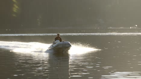 male in motorboat moving at water of alaskan bay on summer evening with sunlight as backlight, slow motion