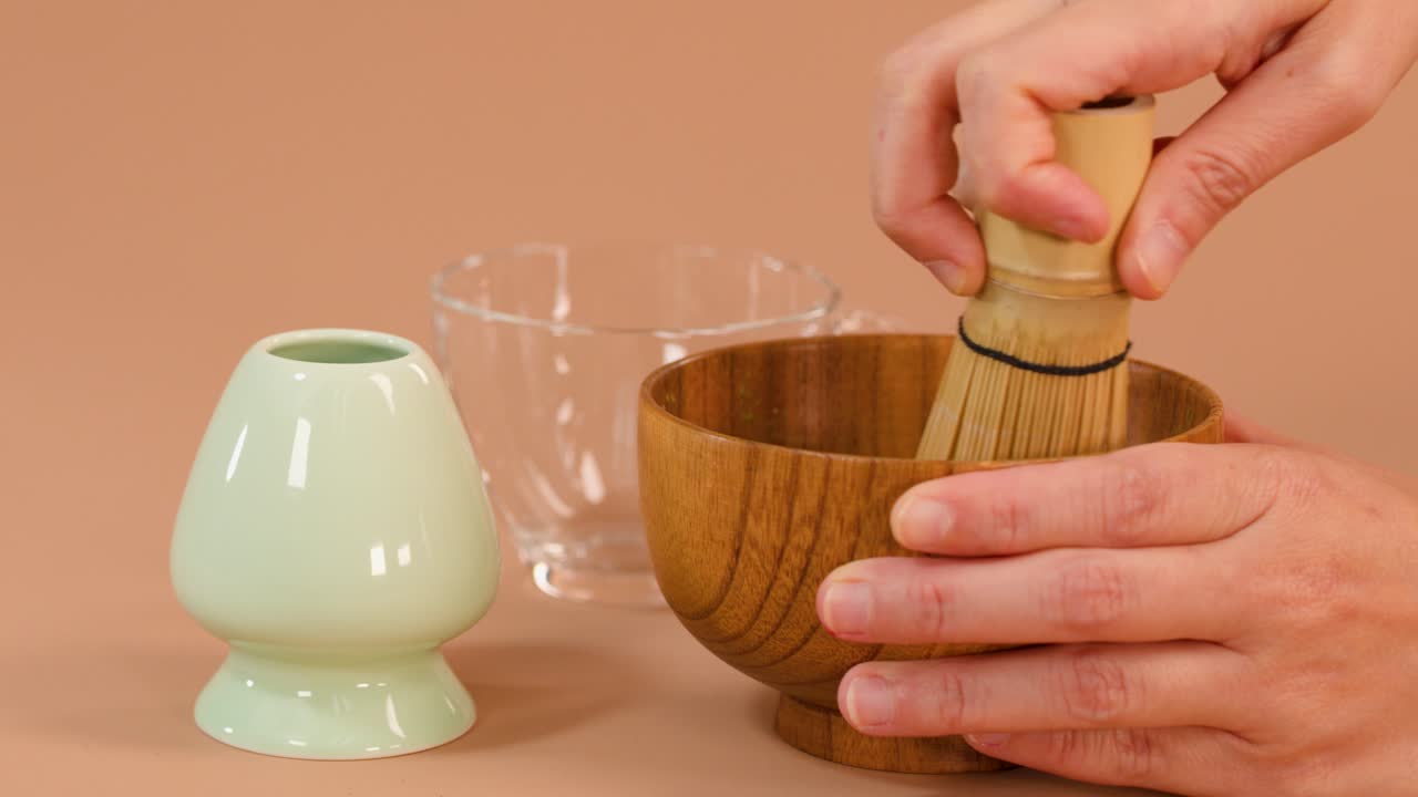 Whisking matcha in wooden bowl, pouring into glass cup, soft lighting, neutral background, steady camera