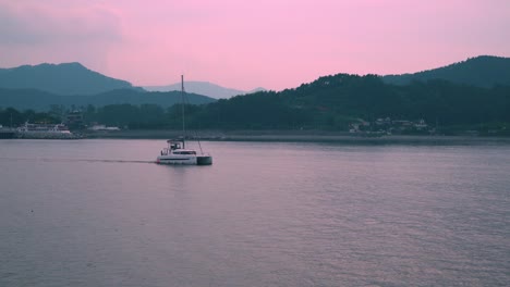 Catamaran-Boat-Cruising-In-The-Ocean-During-Sunset-With-Pink-Sky-In-The-Background