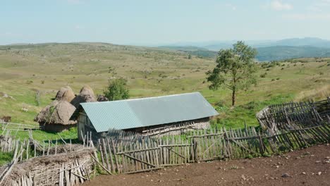 Cottages-With-Wooden-Fencing-On-Meadow-Hilly-Landscape-During-Summer