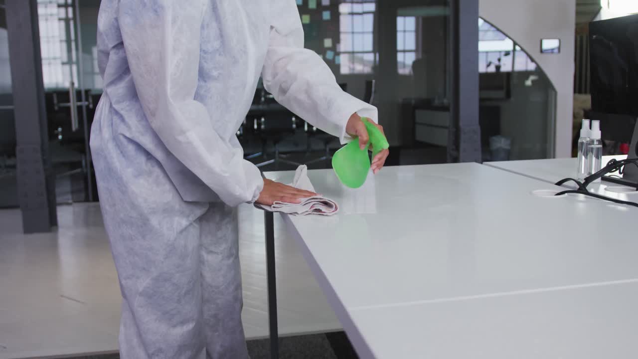 Midsection of cleaner wearing protective overalls disinfecting office and furniture