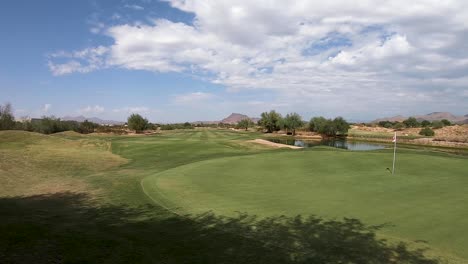 Pan-across-a-distant-green-and-pin,-fairway,-and-water-hazard-at-a-golf-course-in-Scottsdale,-Arizona