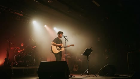 a captivating performance: a solo musician strumming his guitar on stage illuminated by dramatic lighting and a vibrant atmosphere