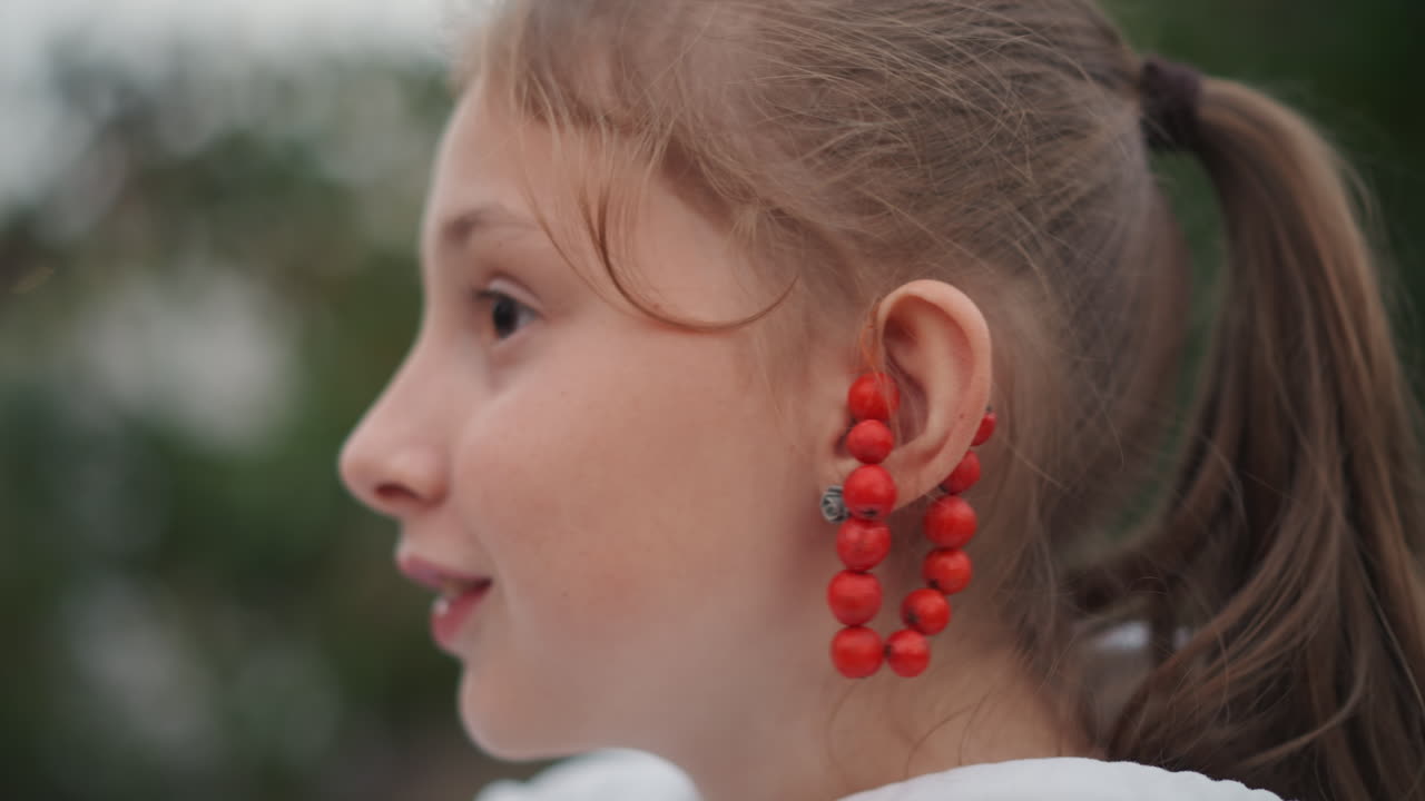 Ragazza con orecchini e coda di cavallo all'aperto. Immagine spontanea di un'attrice che prova le battute sotto il sole. La luce naturale cattura l'espressione sorpresa di una giovane attrice con perline e coda di cavallo all'aperto.