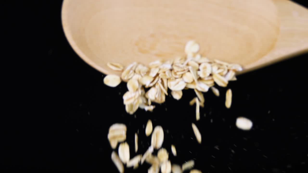 Oats cascade from a wooden spoon in slow motion, set against a dark backdrop, highlighting texture and movement