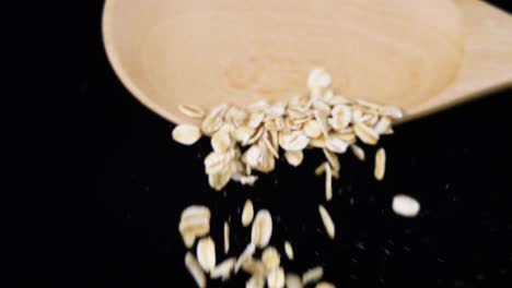 oats cascade from a wooden spoon in slow motion, set against a dark backdrop, highlighting texture and movement